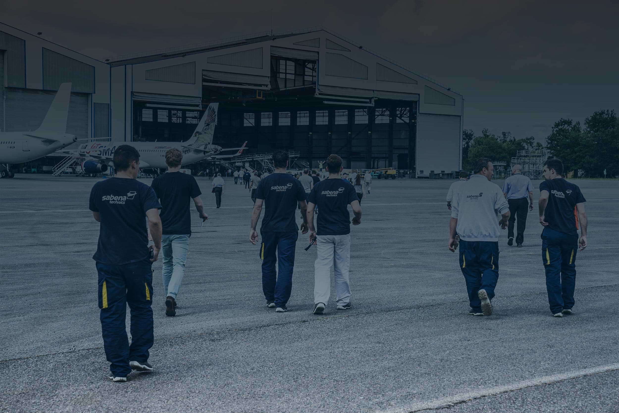 Team of Sabena technics technicians walking toward a hangar on the runway of an aircraft maintenance site